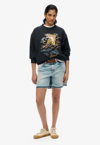 Sudadera navy con bordado de tigre, combinada con pantalones cortos de mezclilla azul claro con dobladillo deshilachado y un ajuste casual, llevada con zapatillas beige.