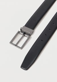 Cinturón de cuero negro con textura suave, que presenta una hebilla metálica rectangular en plata oscura. Múltiples agujeros de ajuste a lo largo de la correa.