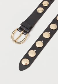 Melnā ādas josta ar zelta dubulto knaģi un lieliem dekoratīviem zelta kniedēm gar siksnu. Gluda virsma ar kontrastējošu šuvumu.