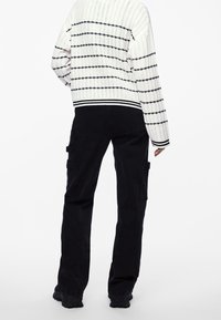 Biały sweter z dzianiny z czarnymi paskami i prążkowanymi mankietami, zestawiony z czarnymi spodniami cargo z kieszeniami i luźnym krojem. Teksturowana powierzchnia.