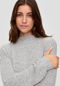 Jasnoszary sweter z wysokim dekoltem i długimi rękawami, wykonany z miękkiego, teksturowanego splotu. Modelka ma skrzyżowane ręce.