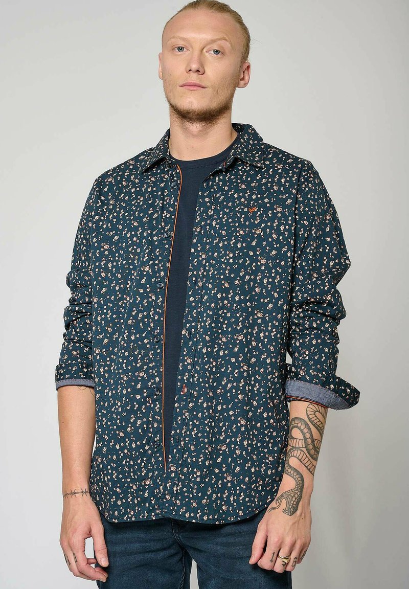 Marineblauw bloemenoverhemd met lange mouwen, met een knoopsluiting aan de voorkant en opgerolde manchetten. Subtiele contrasterende stiksels en een gestructureerde stof.