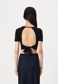 Crni crop top s kratkim rukavima i otvorenim leđima, vezan u struku. Uparen s tamnoplavom čipkastom suknjom koja ima cvjetni uzorak.