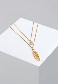 Collana a strati in tono oro caratterizzata da un pendente a forma di cristallo rotondo e un ciondolo a forma di foglia, con dettagli di catena fine e finitura lucida.