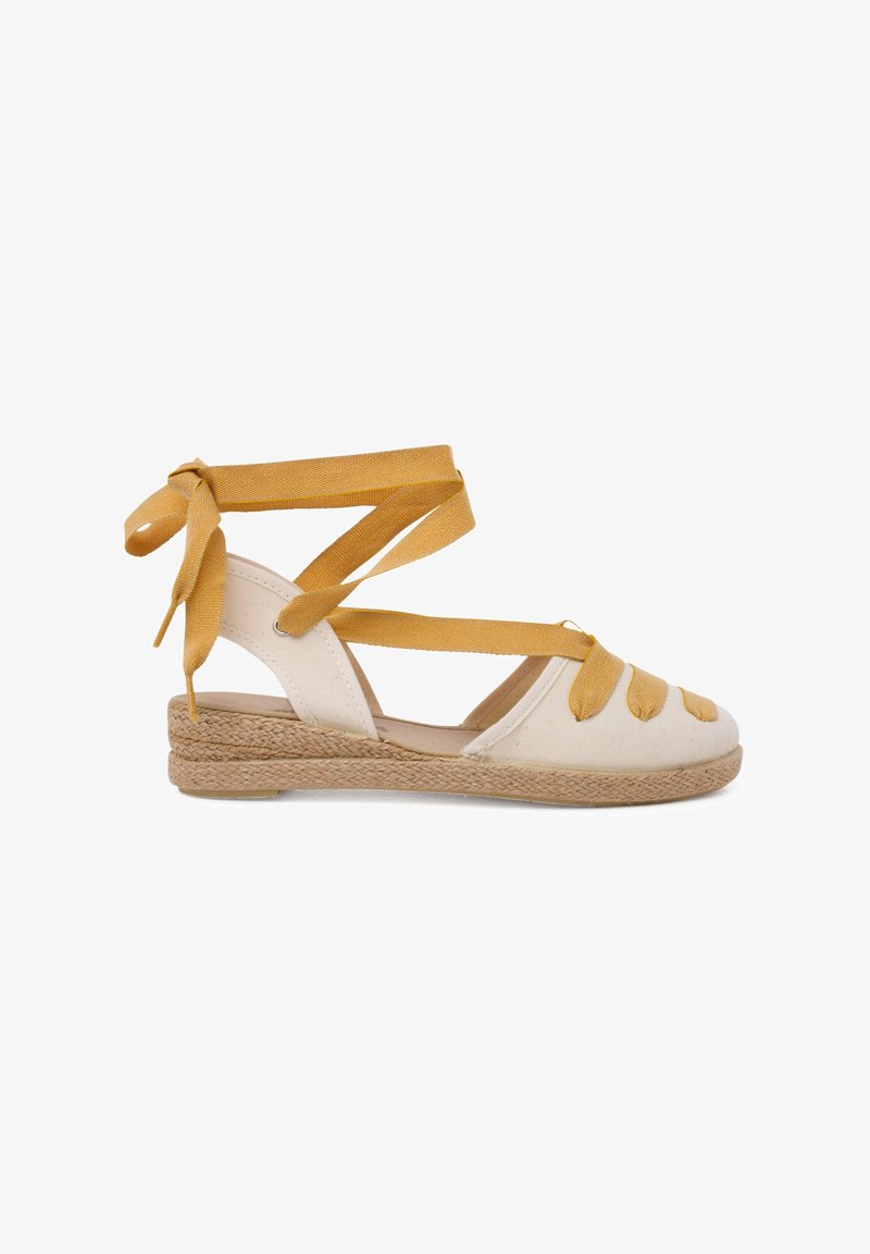 Bílé plátěné espadrilky s pletenou jutu podrážkou, s žlutými látkovými popruhy, které se omotávají kolem kotníku a dekorativními uzlovými detaily.
