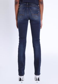 Jeans ajustados de color azul oscuro con una textura suave, que cuentan con dos bolsillos traseros con costuras amarillas y una silueta ajustada hasta los tobillos.