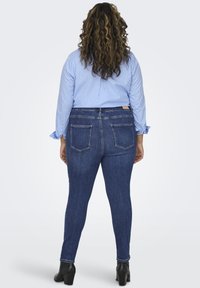 Jeans skinny de color azul oscuro con cintura alta y bolsillos traseros, combinados con una camiseta de manga larga a rayas en azul claro y blanco. Botas negras de tacón.