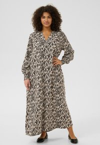 Robe maxi avec un motif géométrique noir et beige, dotée de manches longues, d'un col et d'une coupe décontractée, accompagnée de ballerines noires.
