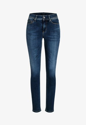 Tummansininen farkkutyyppiset kapeat farkut, joissa on etunappi, vetoketjukiinnitys ja viiden taskun malli, valkoisella taustalla.