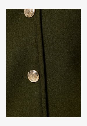 Donkergroen stof met een gladde textuur, voorzien van een opvallende zilveren knop met een reliëfontwerp in het midden.