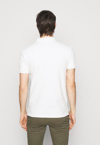 White polo shirt with short sleeves, featuring a classic collar and side slits, paired with olive green pants. Smooth cotton texture.