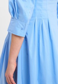 Light blue dress featuring puffed sleeves, a button detail on the cuff, and pleats along the skirt for texture and movement.
