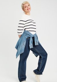 Maglione bianco con righe navy, abbinato a jeans blu a vita alta e una giacca di jeans legata in vita, dal fit rilassato.