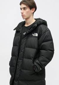 Crna puhasta jakna s patentnim zatvaračem, podstavljenim panelima i kapuljačom. Na prsima i rukavima ima logo The North Face. Mekana tekstura.