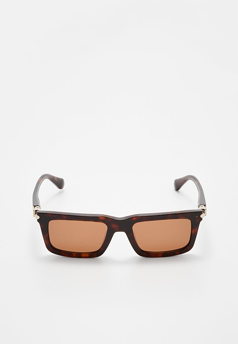 Lunettes de soleil écaille de tortue marron avec des montures carrées, des verres teintés marron et des accents dorés sur les charnières. Fini en plastique lisse.