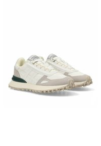Zapatillas blancas con parte superior texturizada en crema y beige, acento verde en el talón y una suela resistente y prominente para mayor tracción.
