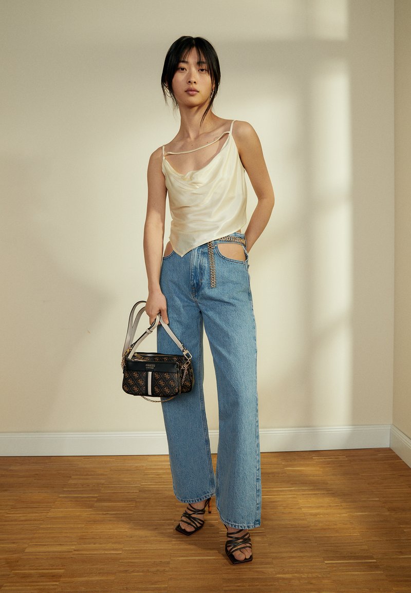 Top de seda com decote drapeado em off-white, jeans de ganga de cintura alta em azul claro, bolsa preta estampada com corrente e sandálias pretas de salto com tiras.