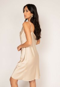 Robe en satin beige avec de fines bretelles spaghetti et une coupe ample, présentant une texture lisse et un ourlet en dentelle. Aucun motif ni quincaillerie notables.