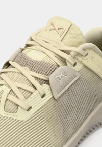 Αθλητικό παπούτσι σε ανοιχτό μπεζ απόχρωση με υφασμάτινη επιφάνεια και ριβντί σχέδιο, που διαθέτει αντίστοιχους κορδόνια και μορφοποιημένη λεπτομέρεια στη γλώσσα.