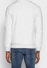 Light gray sweatshirt made of soft fabric with ribbed cuffs and hem, featuring black accents along the shoulders, worn with blue jeans.