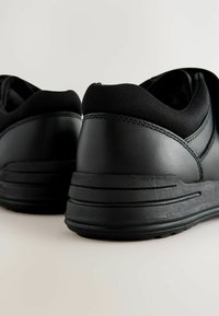 Baskets noires avec des accents en cuir lisse et en tissu, dotées d'un col rembourré, d'une semelle texturée et de détails de couture contrastants.