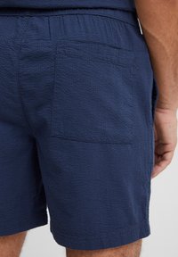 Granatowe szorty wykonane z teksturowanej tkaniny, wyposażone w elastyczny pas i jedną tylną kieszeń. Obszycie na dole jest starannie wykonane.