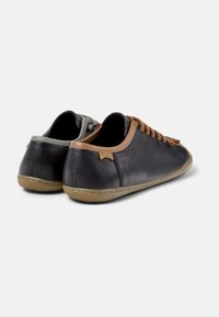 Schwarze Leder-Sneaker mit braunen Schnürsenkeln und einem sandfarbenen Akzent an der Ferse. Das Design ist schlicht, mit einer minimalistischen Ästhetik und Gummisohlen.