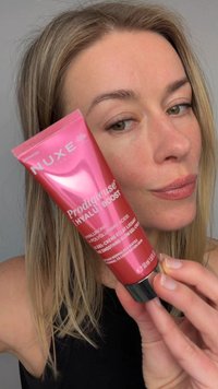 Femme aux cheveux châtain clair tient un tube rose de gel-crème éclat lissant NUXE Prodigieuse Hyalu Boost près de son visage.