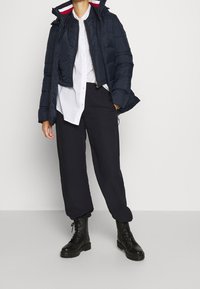 Granatowa pikowana kurtka puchowa z zamkiem i kapturem, zestawiona z białą koszulą na guziki i czarnymi luźnymi spodniami, uzupełniona czarnymi wojskowymi butami.