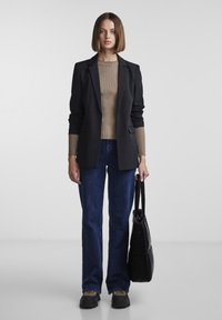 Črn blazer preko rebraste bež puloverja, v kombinaciji s prema straight-leg modrimi kavbojkami. Črna torba preko rame in robustni črni čevlji zaokrožijo videz.