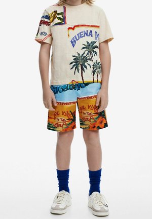 Short-sleeve beige shirt with colorful graphics, palm trees, and text, paired with patterned shorts in blue and orange. Blue socks and white sneakers.