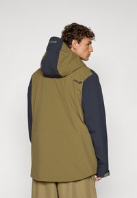 Giacca verde oliva e blu navy con cappuccio, caratterizzata da una finitura opaca e un design minimalista. Marchio discreto sul retro.
