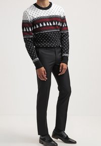 Stickad tröja i vitt, svart och rött med vinterträdsmönster; kombinerad med svarta kostymbyxor och klassiska svarta skor.