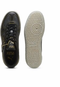 Mustad mustad nahkketsid kollaste õmblustega, reljeefsete kummitaldadega ja silmapaistva logo detailiga disain.