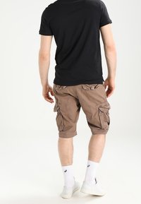 Pantalones cortos cargo marrones con múltiples bolsillos laterales, un ajuste relajado y un dobladillo vuelto, combinados con calcetines blancos y zapatillas blancas.