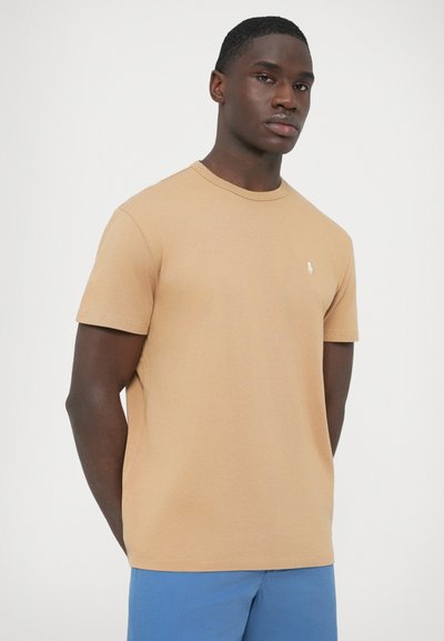 Barna, pamut anyagból készült, kereknyakú póló, rövid ujjakkal és a mellkason kis hímzett logóval. Simább tapintású, testhezálló fazon.