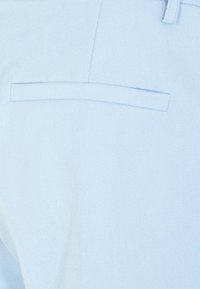 Tissu bleu clair à texture lisse. Dispose d'une poche arrière horizontale avec une ouverture plate. Le matériau présente un motif de tissage subtil.