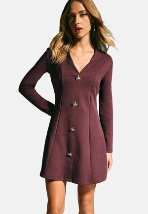 Vestido burdeos de manga larga, escote en V y acentos de botones en tono dorado a lo largo del frente. Tejido de textura suave con una silueta ajustada.