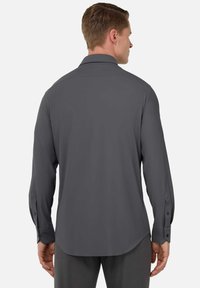Camisa gris de manga larga con una textura suave y mate, cuello estructurado y puños abotonados; presenta un dobladillo curvado y un diseño minimalista.