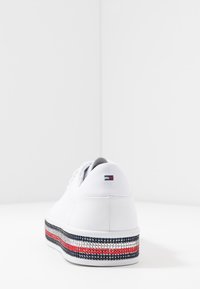 Białe skórzane tenisówki z teksturowaną platformą, zdobioną czerwonymi, białymi i niebieskimi paskami. Okrągły obcas i minimalistyczne elementy projektu.