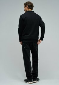 Sudadera negra con cuello redondo, puños y dobladillo acanalados, combinada con vaqueros de mezclilla oscuros. Costuras visibles y bolsillos en los vaqueros.