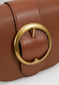 Brun läderhandväska med ett runt lås i guldfärg med en ögla, texturerad yta och subtila sömnadsdetaljer.