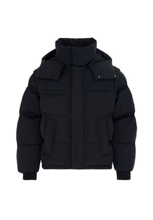 Homme portant une doudoune noire, un pantalon noir avec une chaîne, des baskets noires et blanches, des lunettes de soleil et une chemise rayée noire et bordeaux sur fond gris.