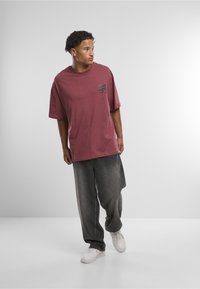 Překrásné oversized fialové tričko s čtvercovým potiskem na hrudi, doplněné tmavě šedými širokými džíny a bílými teniskami. Hladká textura látky.