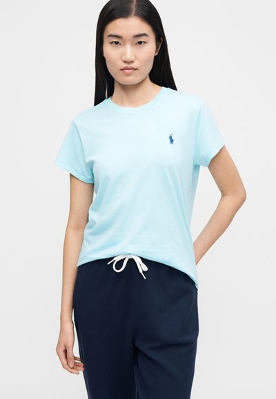 Gaiši zils kokvilnas T-krekls ar īsām piedurknēm un apaļu kakla izgriezumu, uz krūtīm neliels tumši zils logo. Saskaņots ar tumšām sporta biksēm.