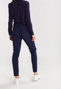 Navy nieco dopasowane spodnie uszyte z gładkiego materiału, posiadające kieszenie i zestawione z białymi sneakersami.