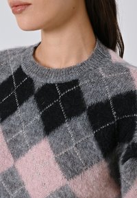 Donna che indossa un maglione a rombi in maglia pelosa, nero, grigio e rosa, con colletto a coste, mostrata dalla spalla al collo.