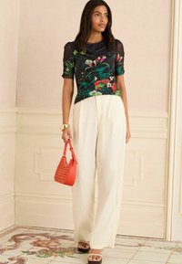Top a stampa floreale nera con accenti verdi e rosa; pantaloni beige a gamba larga; borsa intrecciata rossa; scarpe con plateau in legno.