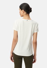 Camiseta blanca de algodón con manga corta y cuello redondo. Textura suave con una etiqueta de logo sutil en la parte de atrás. Combinada con pantalones de color verde oliva.