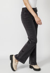 Crne kordura hlače s oblikom u obliku zvona, s dva prednja džepa i visokim strukom. Model nosi bež platforme loafers.